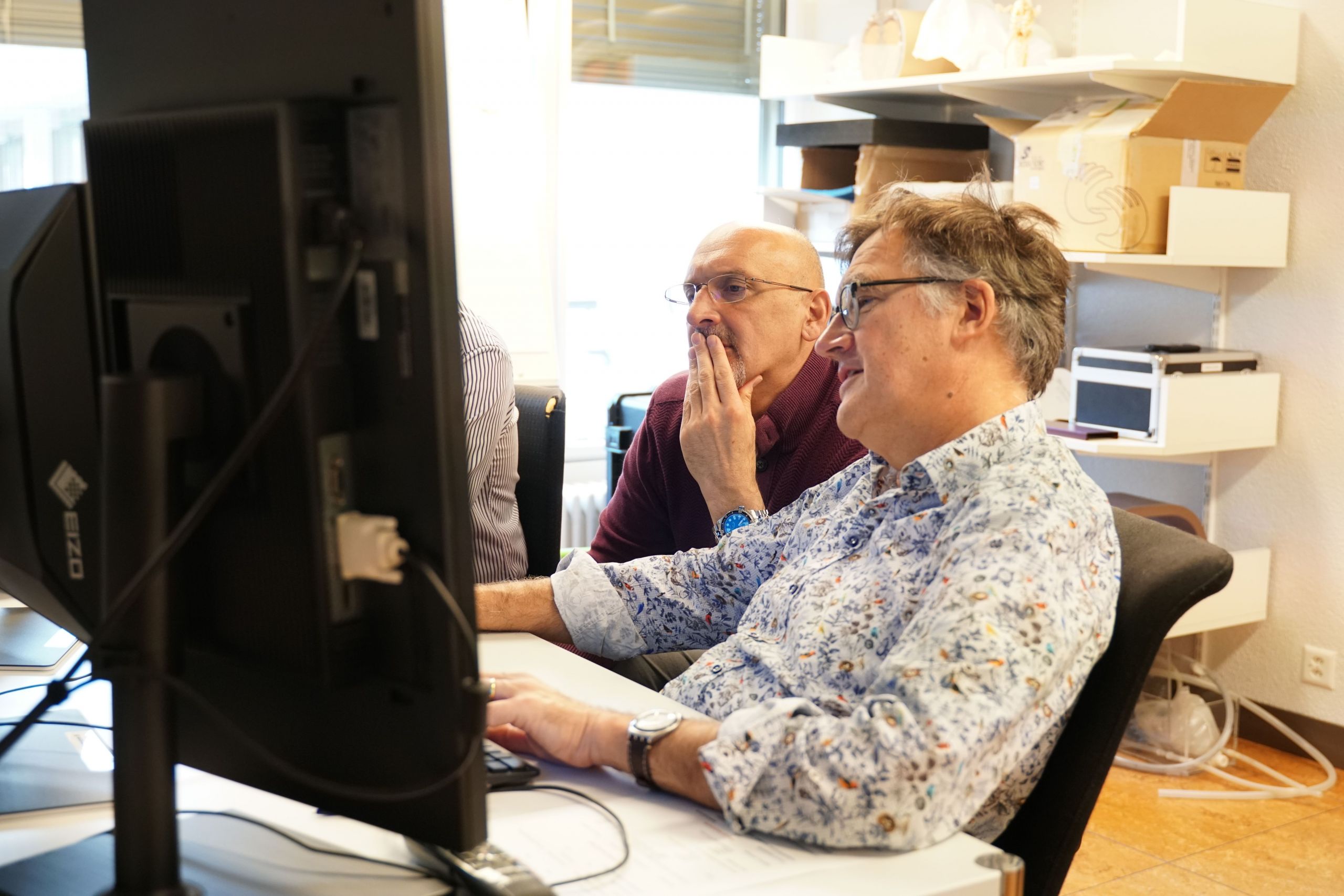Zwei Männer sitzen an einem Computer und bereden etwas