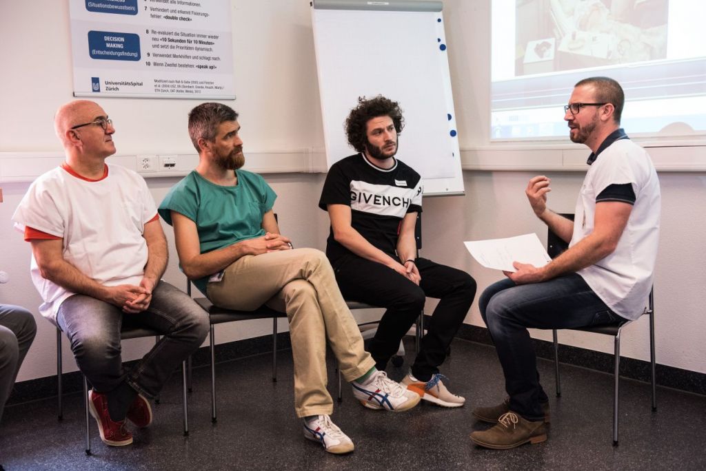 Ein Leiter und drei Zuhörer in einem Raum beim Briefing zur Simulation