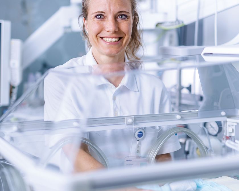Eine Frau steht lächelnd vor einer Babystation