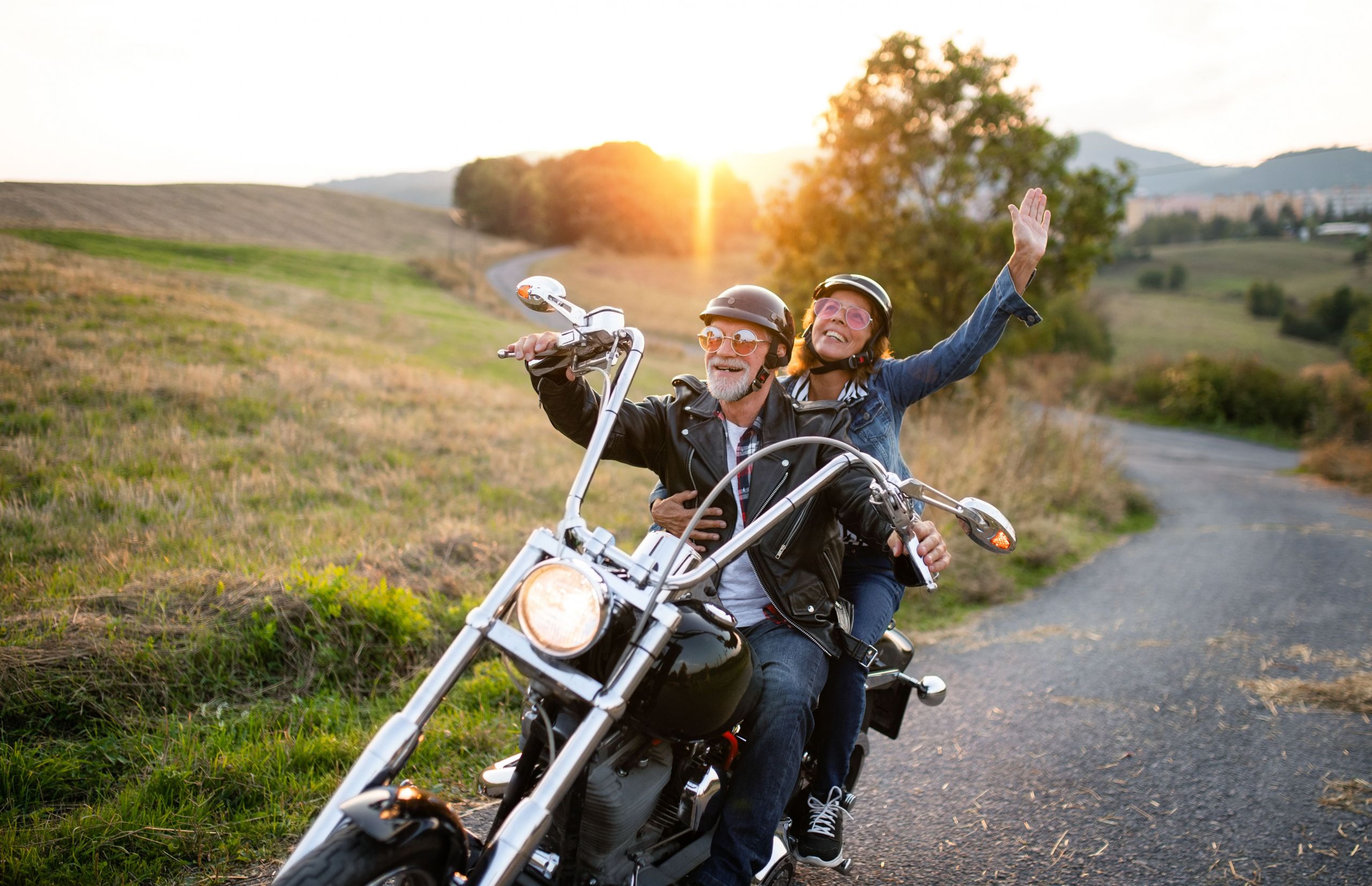 Ein Mann mit seiner Frau fahren auf einem Motorrad durch eine Landschaft bei Sonnenuntergang