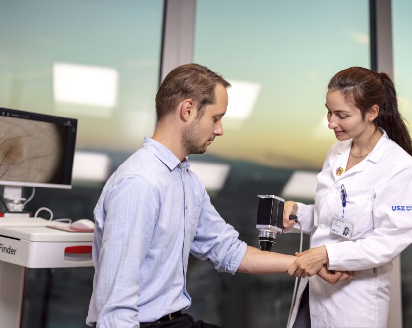 Eine Ärztin untersucht einen Patienten mit einem Auflichtmikroskop.