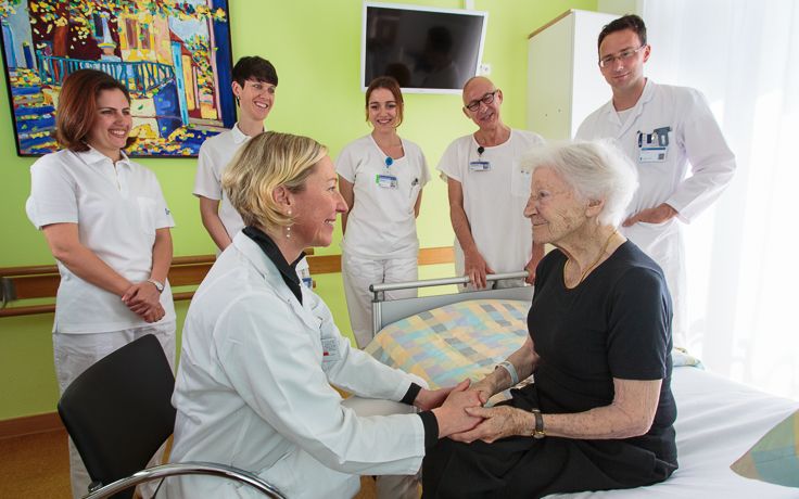 Das Pflegeteam der Geriatrie steht um eine ältere Dame