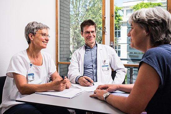 Ein Arzt und eine Pflegerin unterhalten sich an einem Tisch mit einer Patientin