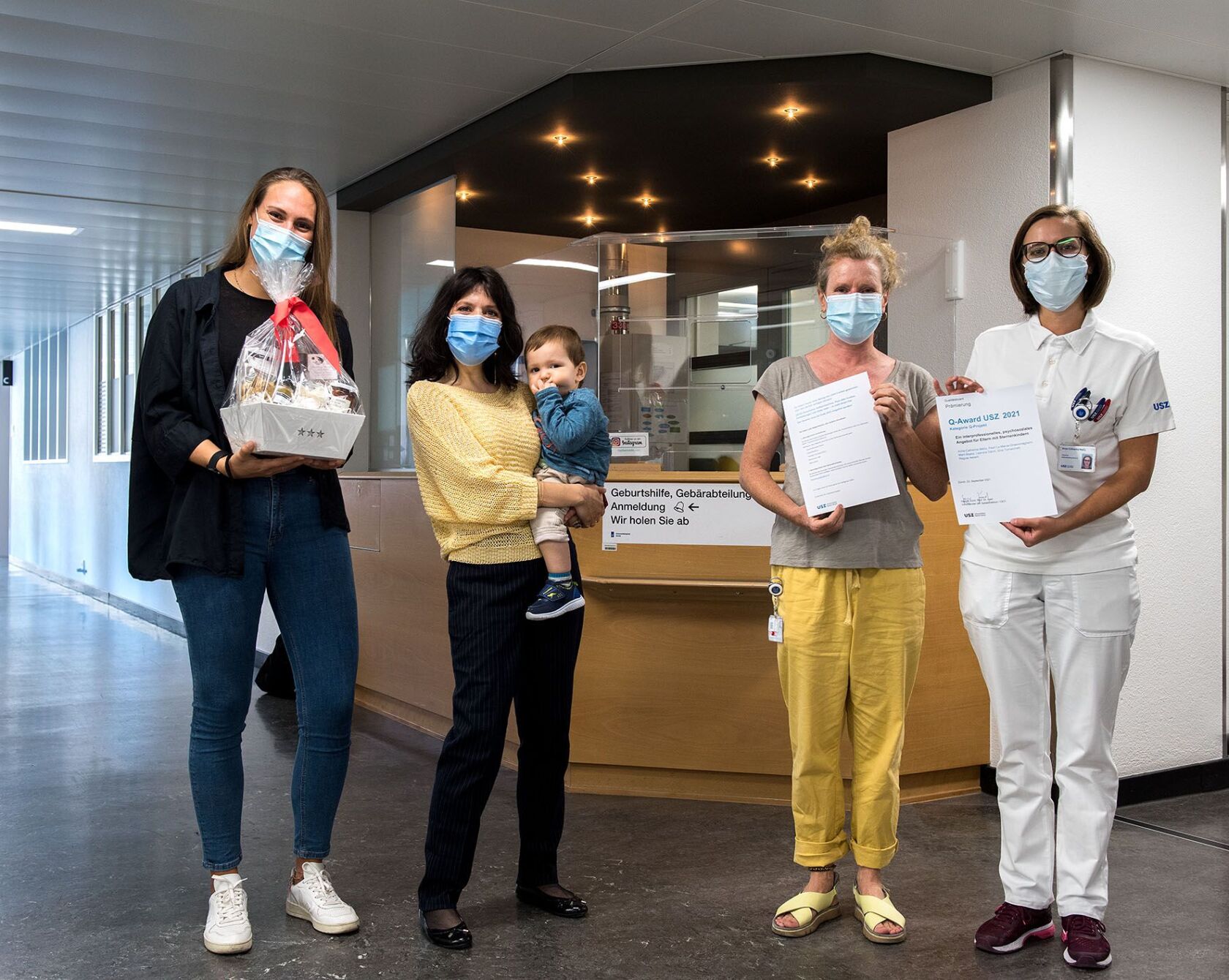 Team steht im Empfangsbereich der Geburtshilfe mit Blumenstrauss und Award